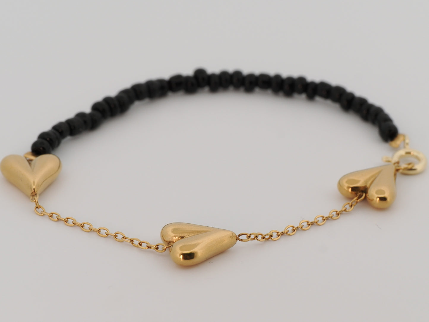 Black beaded bracelet with gold heart-shaped charms on a light gray background