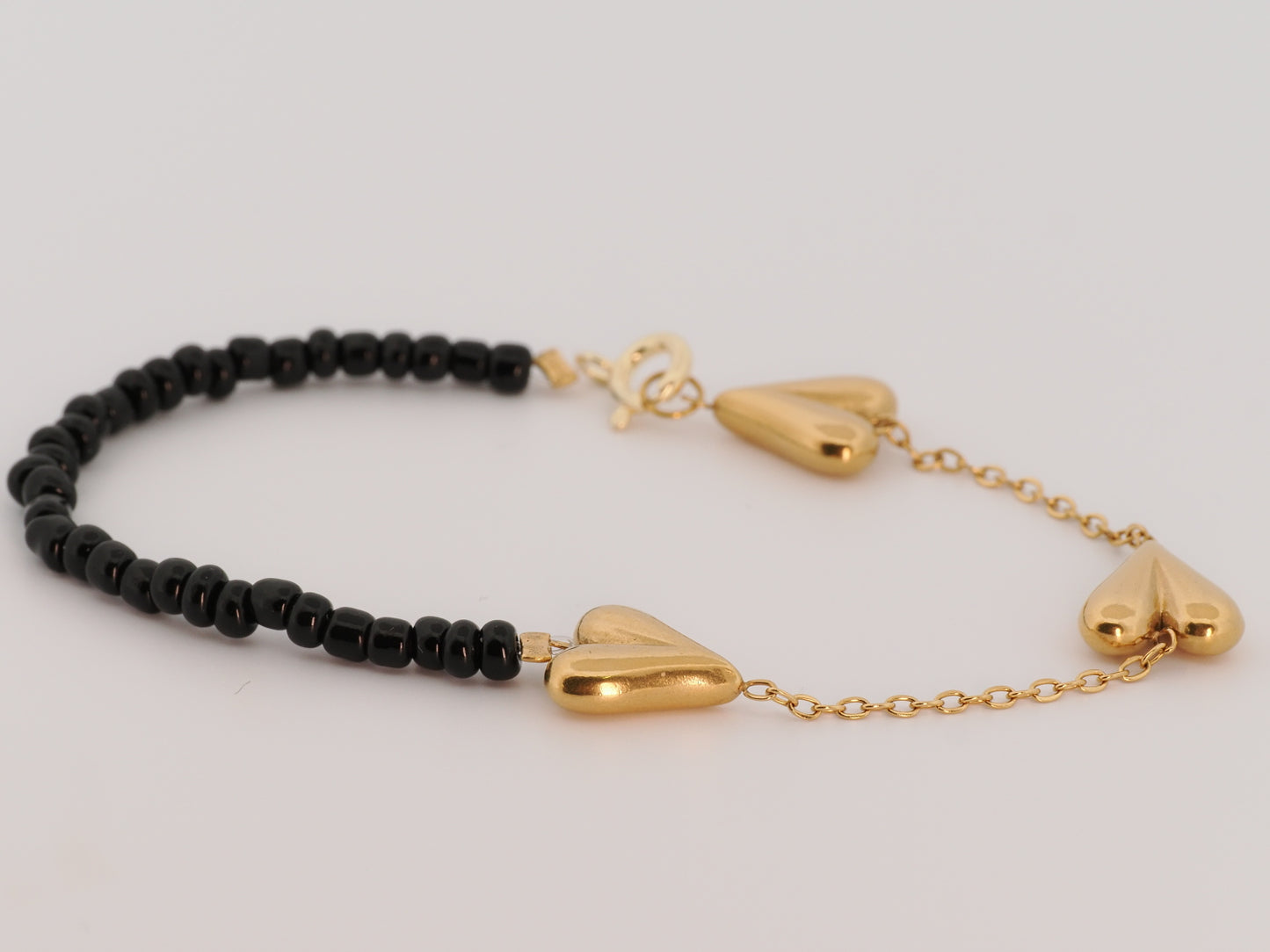Bracelet with black beads and gold heart-shaped clasps on a light gray background