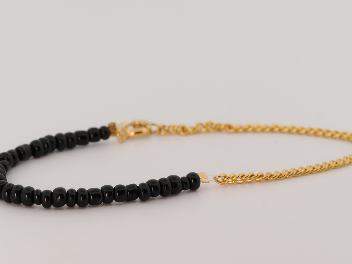 Black beaded necklace with gold chain on a light gray background