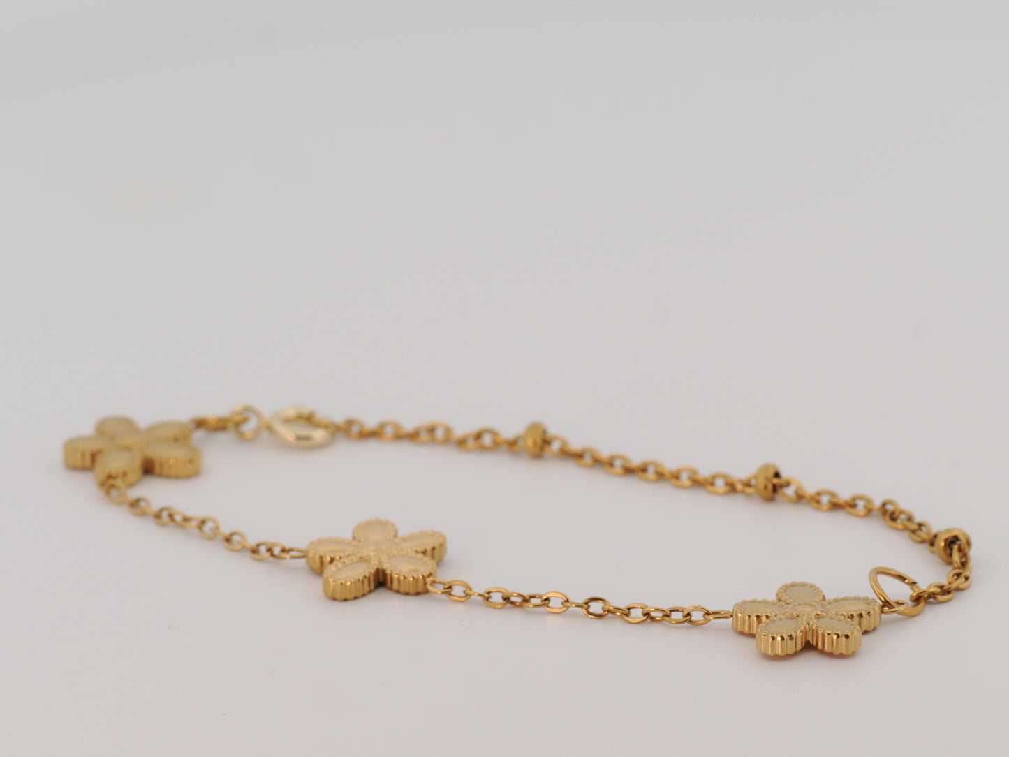 Gold bracelet with clover-shaped charms on a light gray background