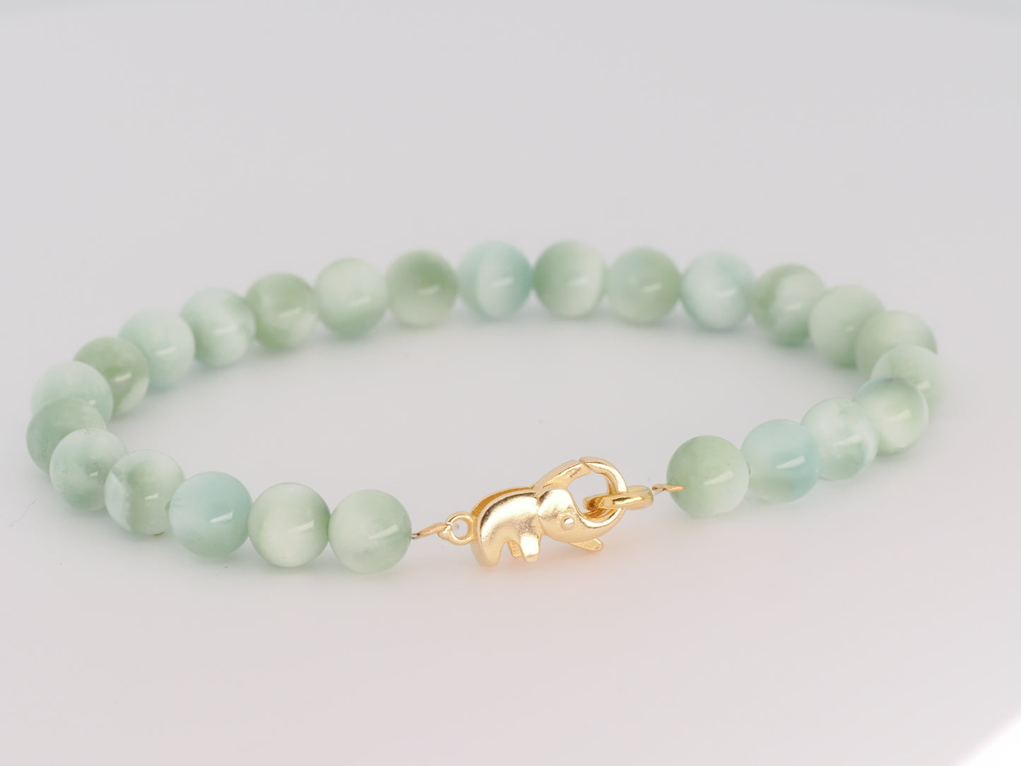 Green beaded bracelet with a gold clasp on a light gray background