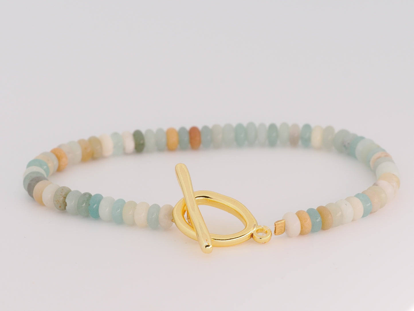 Multicolored beaded bracelet with a gold toggle clasp on a light gray background