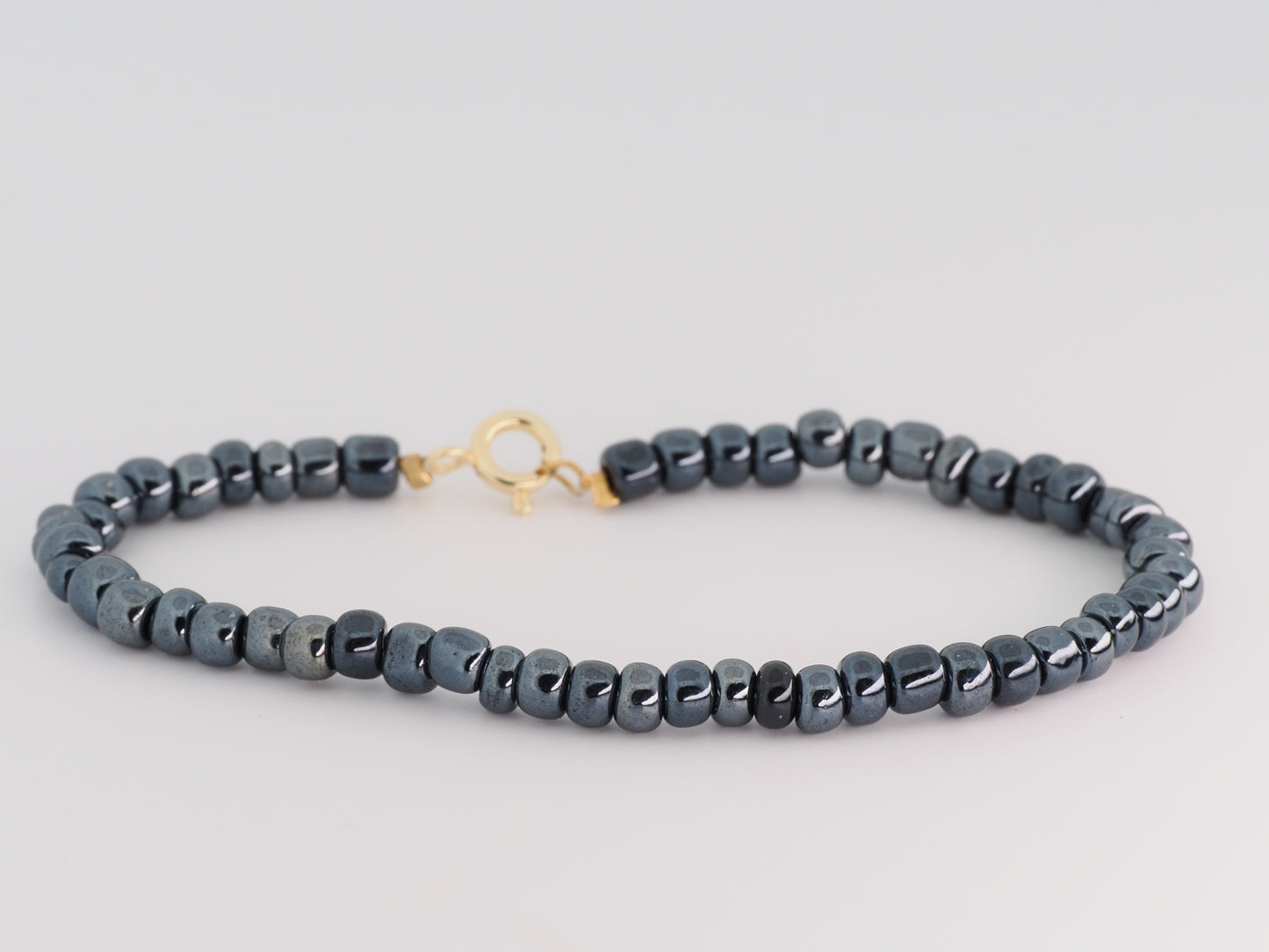 Gray beaded necklace with a gold clasp on a light gray background