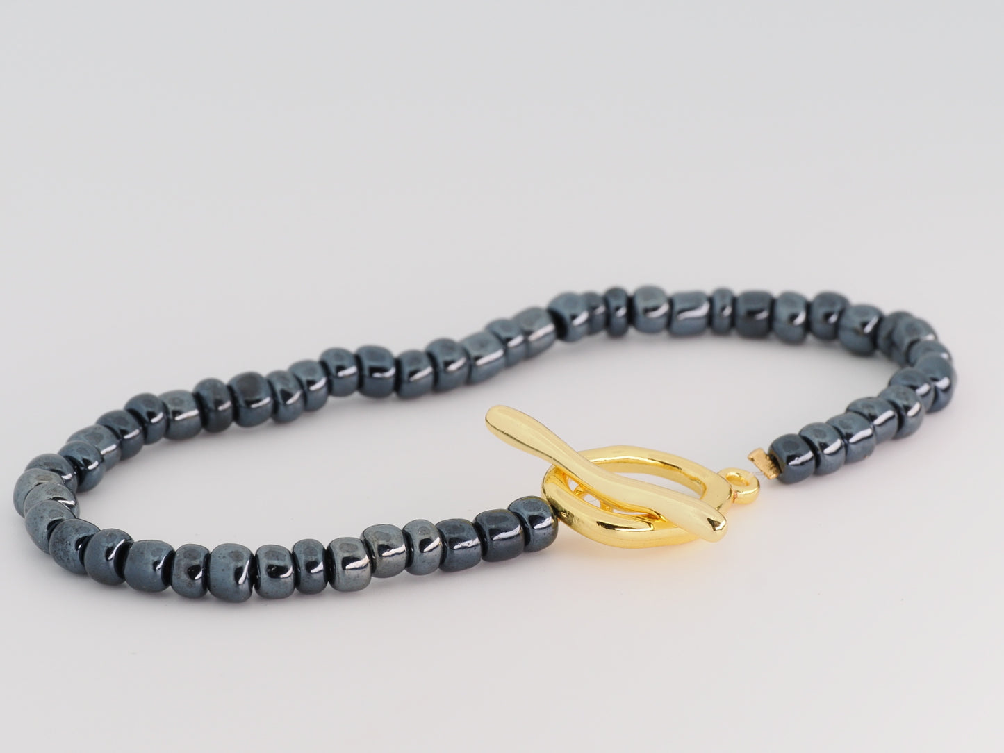 Gray beaded bracelet with a gold clasp on a light gray background