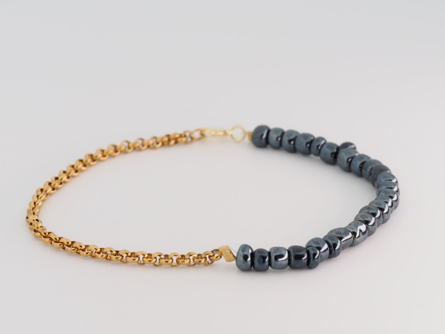 Bracelet with gold chain and dark beads on a light gray background