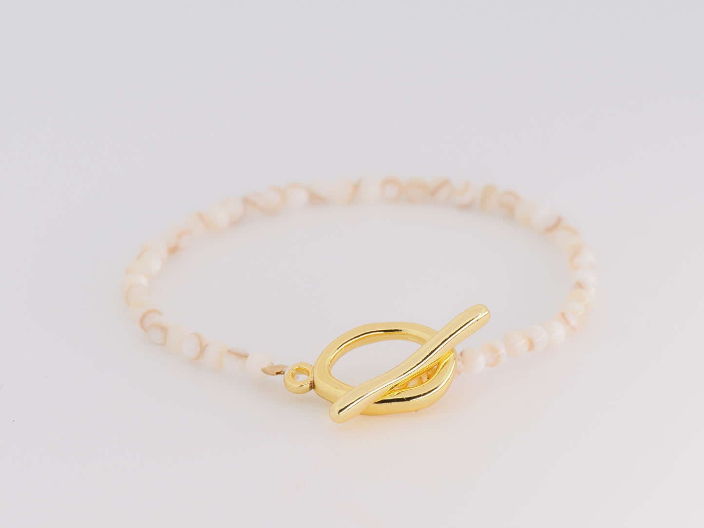 Gold bracelet with a unique clasp on a light gray background