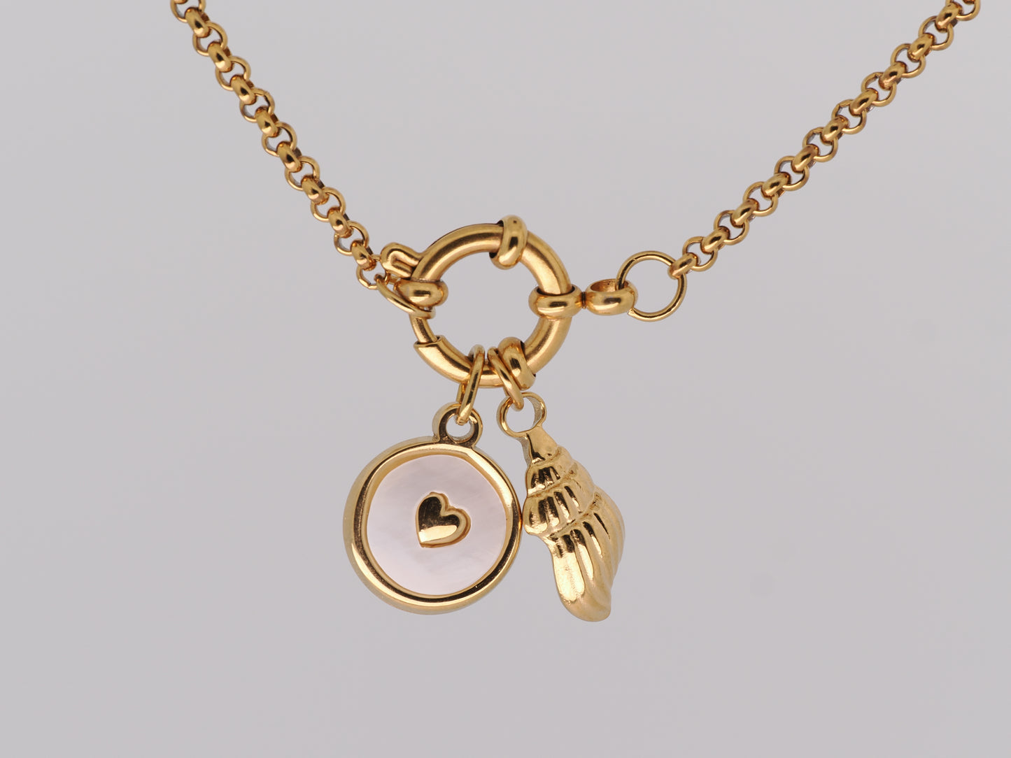 Gold necklace with heart and shell charms on a light gray background