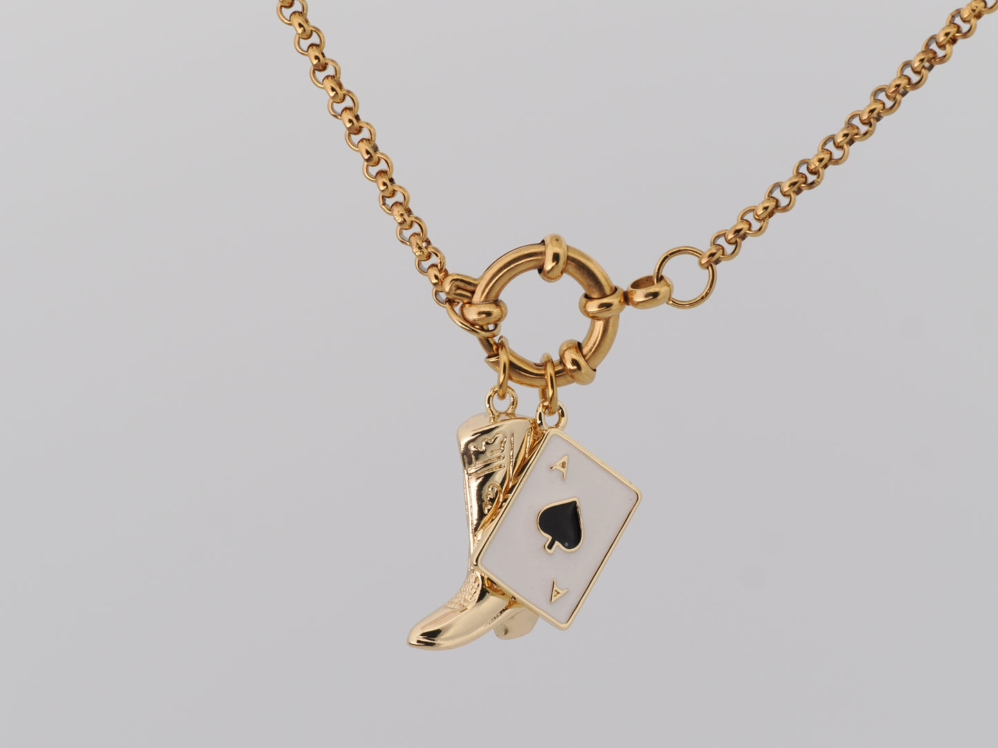 Gold necklace with a boot and card charm on a gray background