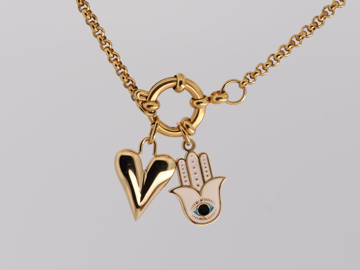 Gold necklace with heart and Hamsa hand pendant on a gray background