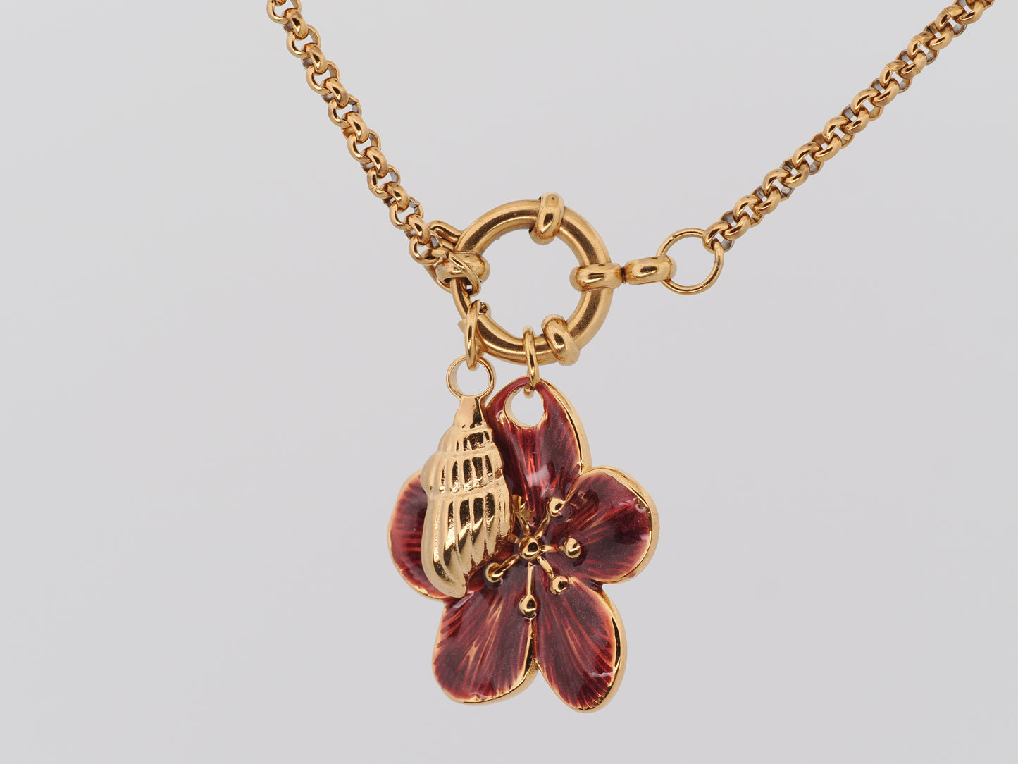 Gold necklace with a red flower pendant on a light gray background