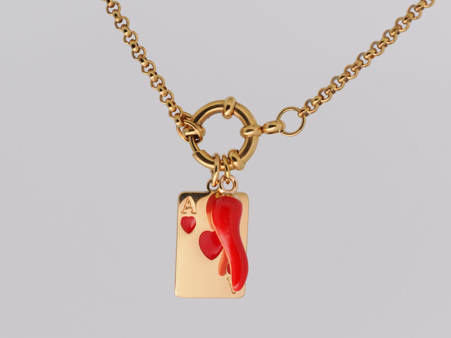 Gold necklace with a red heart and card charm on a gray background