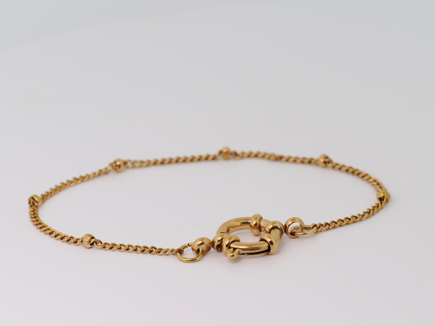 Gold bracelet with a clasp on a light gray background