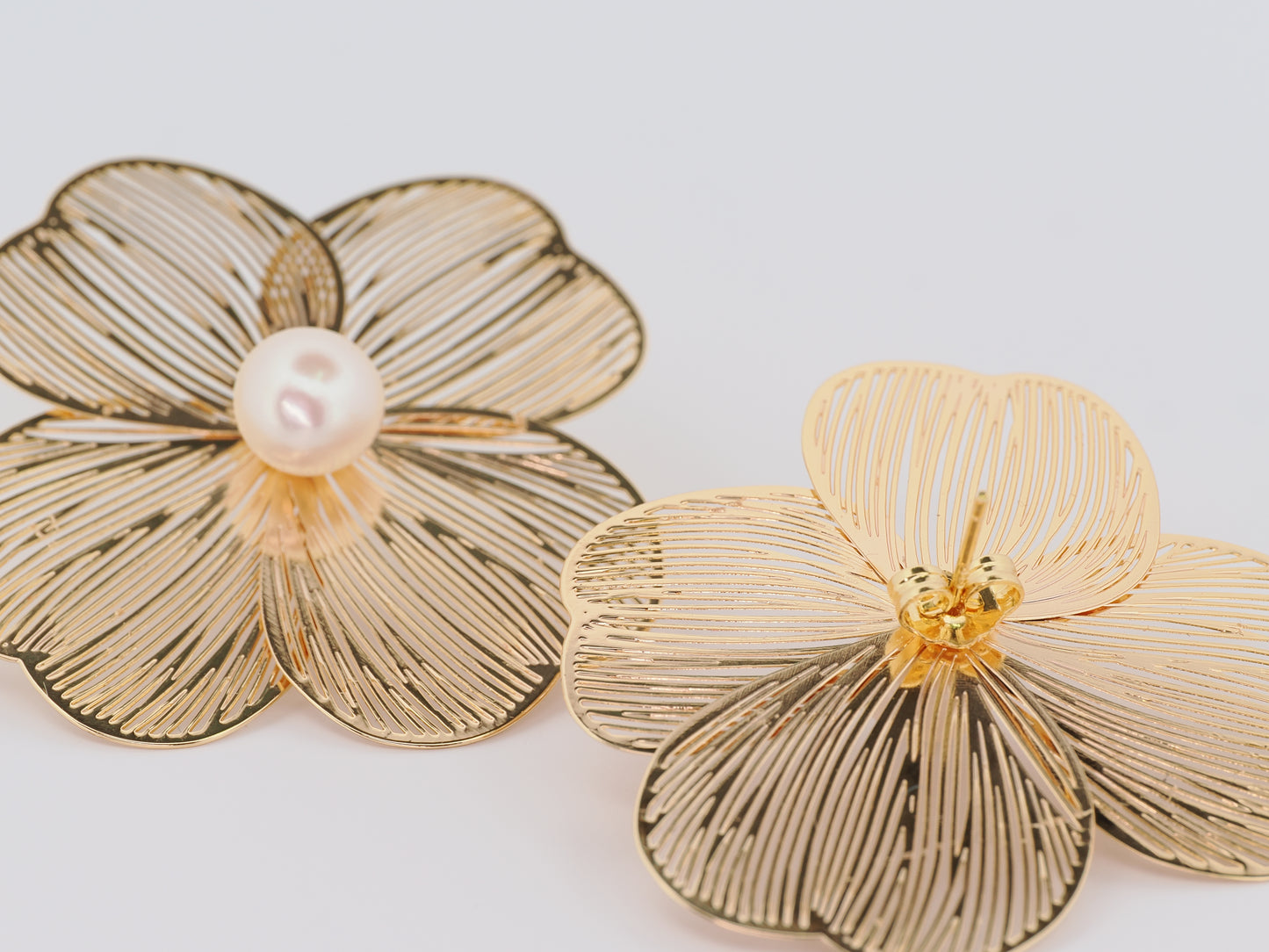 Gold flower-shaped earrings with a pearl center on a light gray background