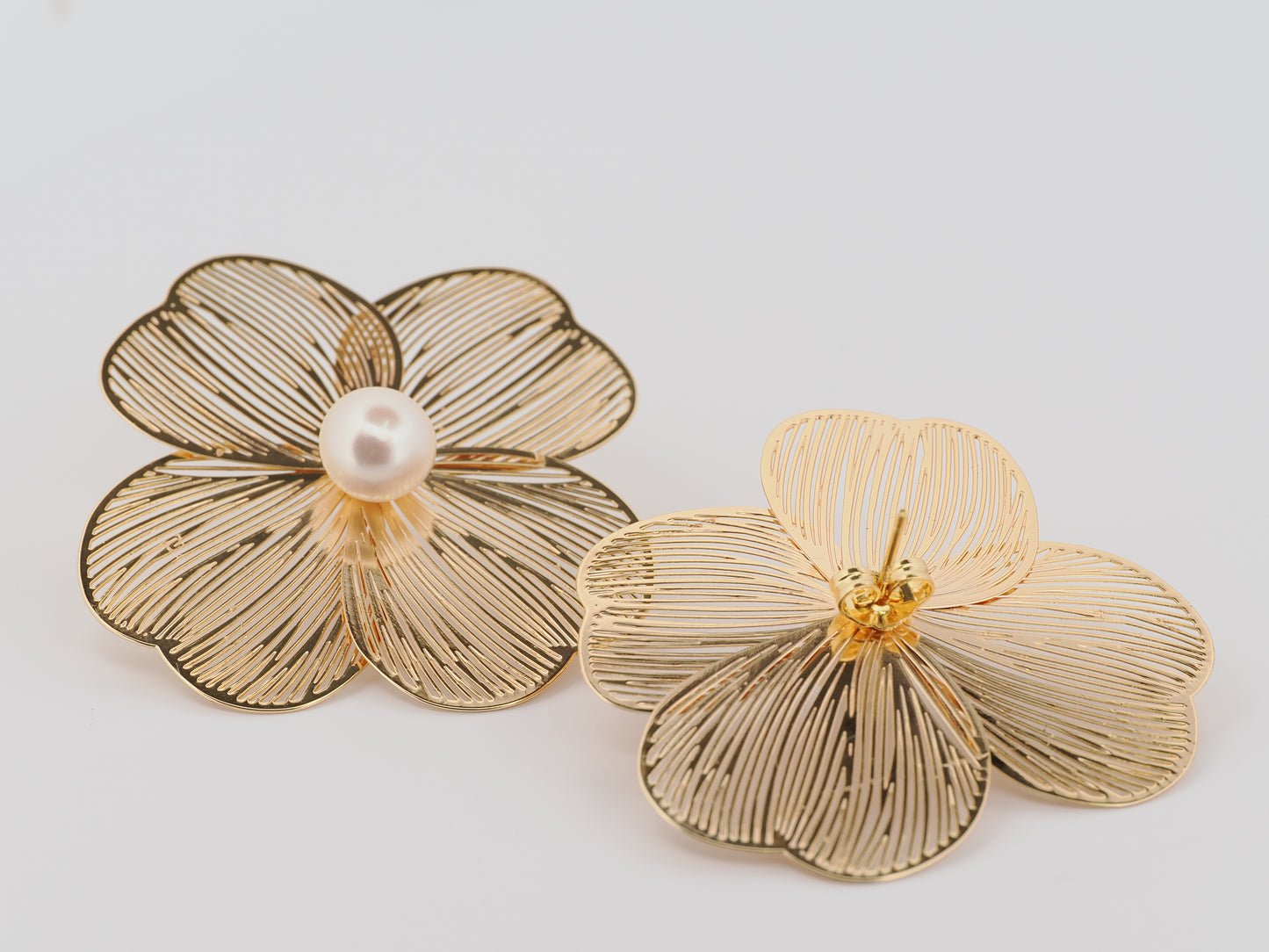 Gold flower-shaped earrings with pearl and yellow center on a light gray background
