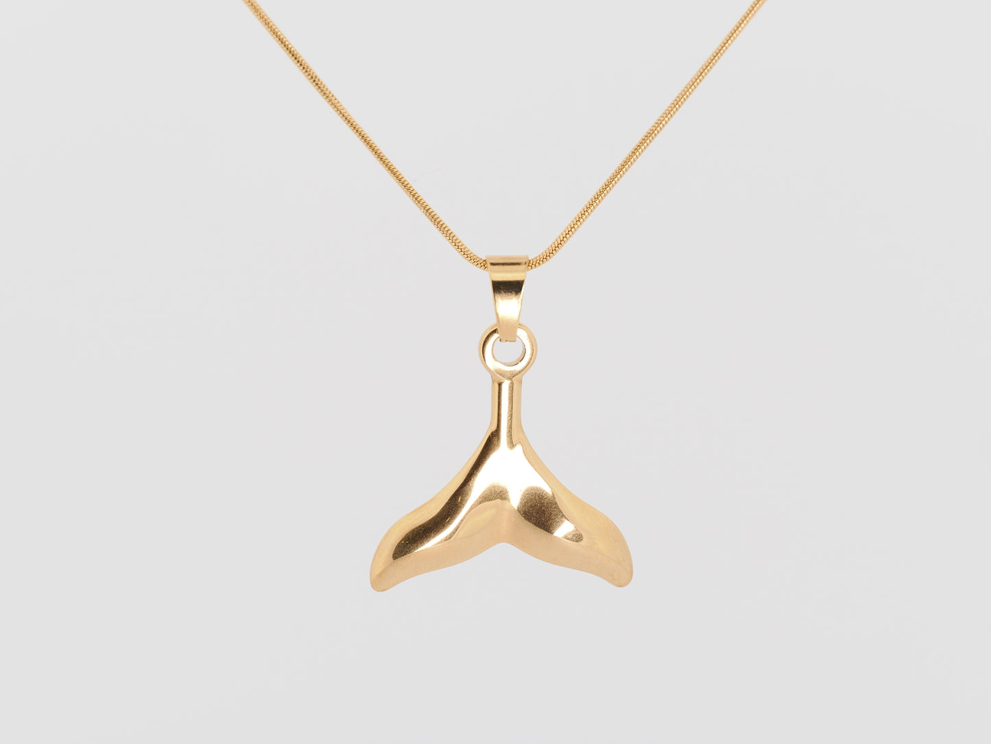 Gold whale tail pendant on a gold chain against a light gray background