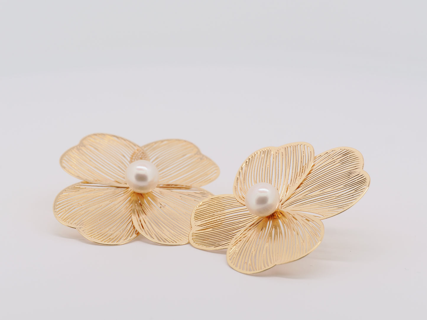Gold flower-shaped earrings with pearls on a light gray background