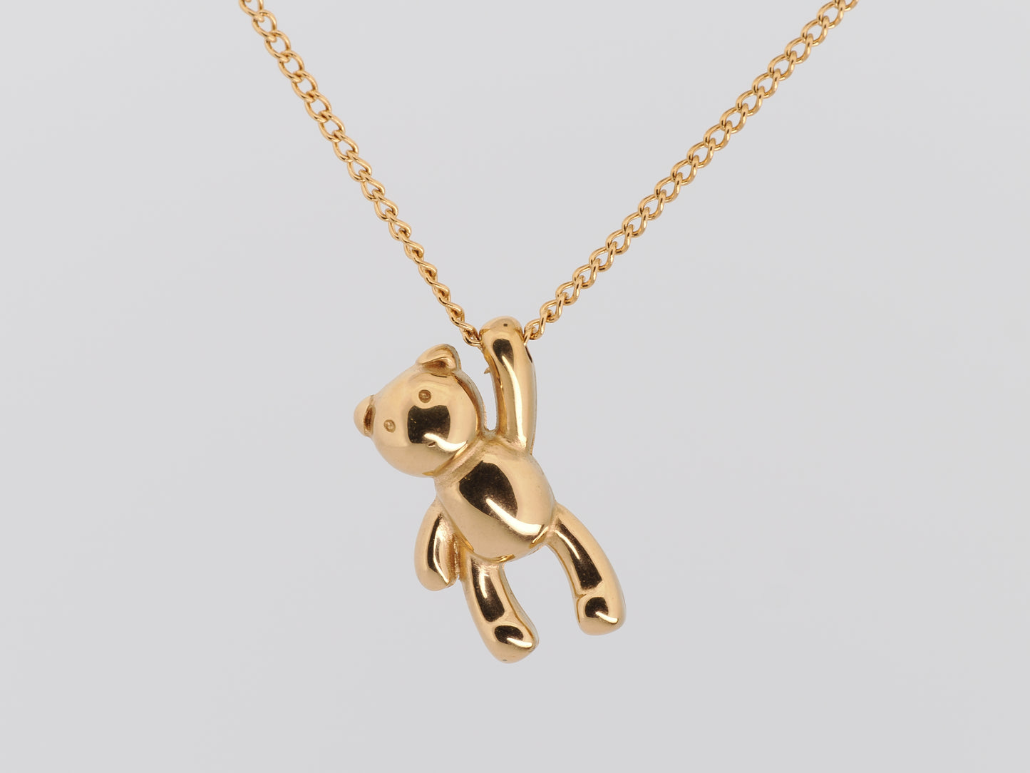Gold teddy bear pendant on a chain against a light gray background