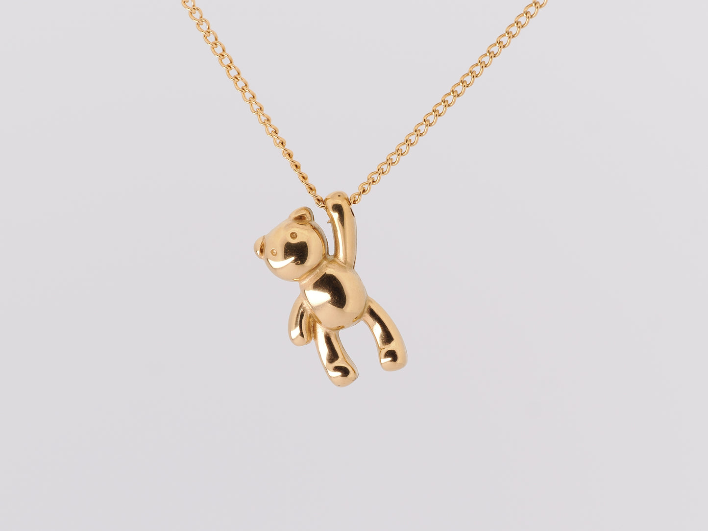 Gold teddy bear pendant on a chain against a light gray background