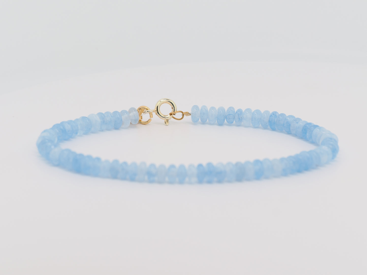 Light blue beaded bracelet with a gold clasp on a light gray background