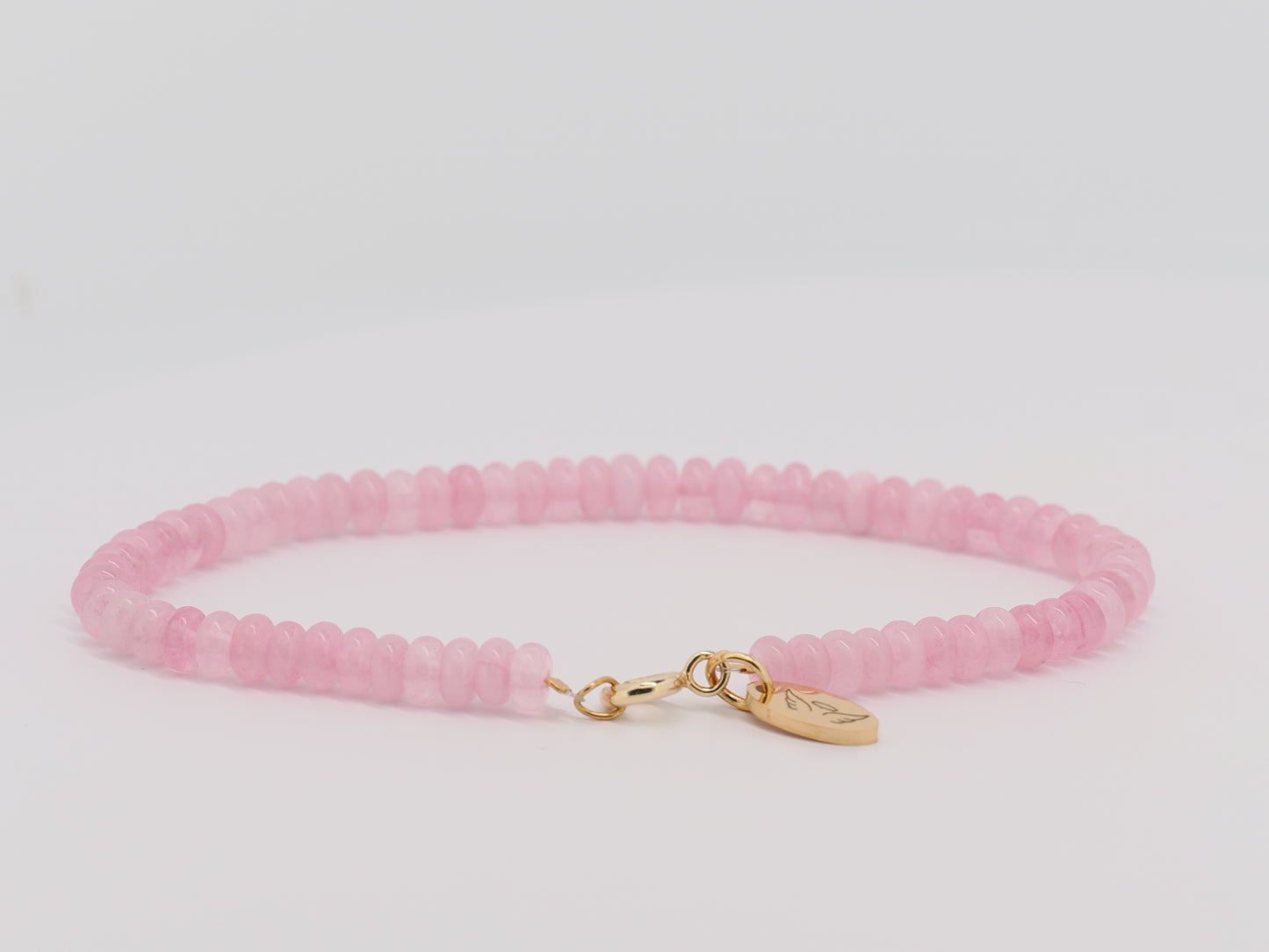 Pink beaded bracelet with a gold charm on a light gray background