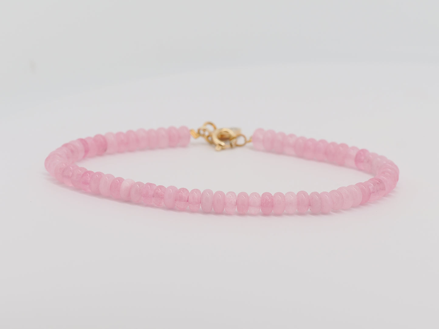 Pink beaded bracelet with a gold clasp on a light gray background