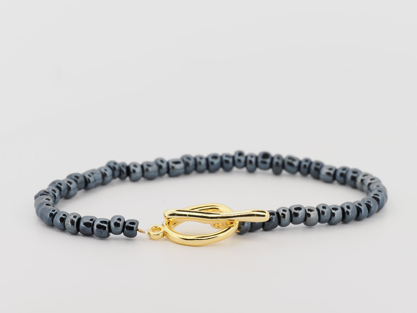 Gray beaded bracelet with a gold clasp on a light gray background