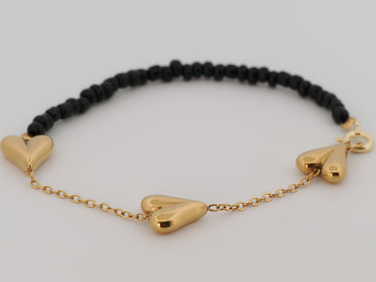 Black beaded bracelet with gold heart-shaped charms on a light gray background