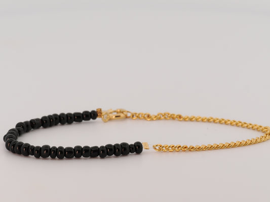 Black beaded bracelet with gold chain on a light gray background