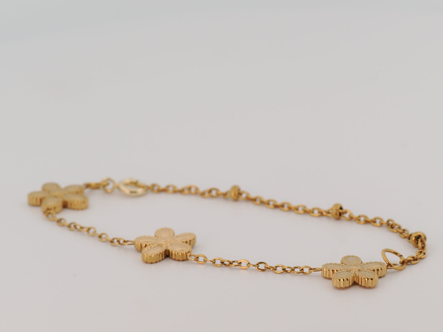 Gold bracelet with clover-shaped charms on a light gray background
