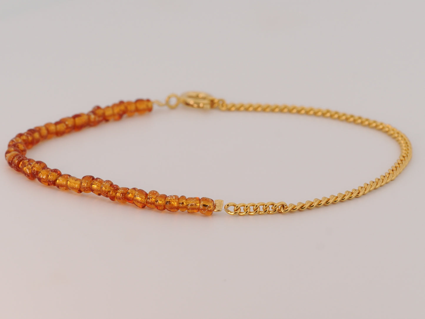 Gold bracelet with orange beads on a light gray background