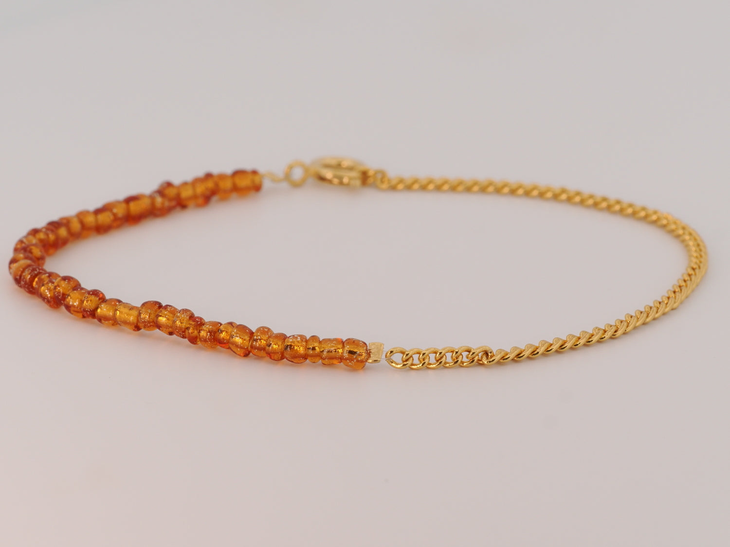 Gold bracelet with orange beads on a light gray background