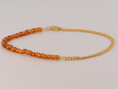 Gold bracelet with orange beads on a light gray background