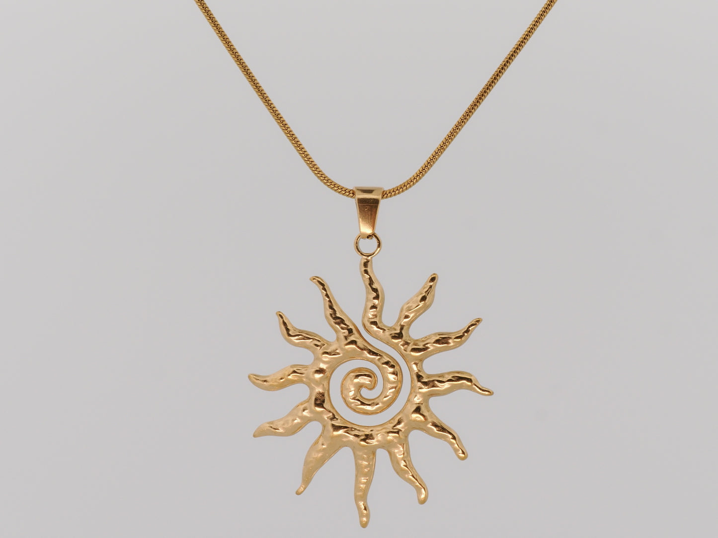 Gold sun-shaped pendant on a chain against a gray background