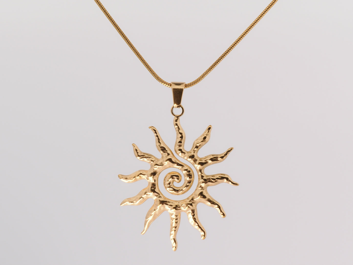 Gold sun-shaped pendant on a chain against a light gray background