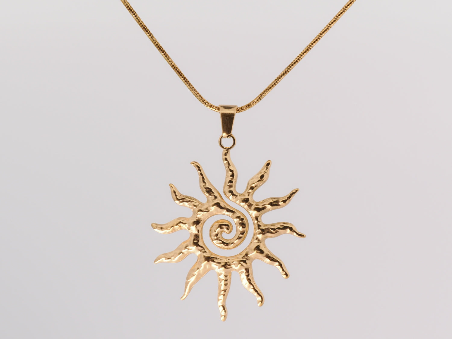 Gold sun-shaped pendant on a chain against a light gray background