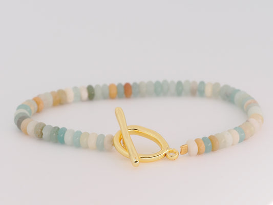 Multicolored beaded bracelet with a gold toggle clasp on a light gray background