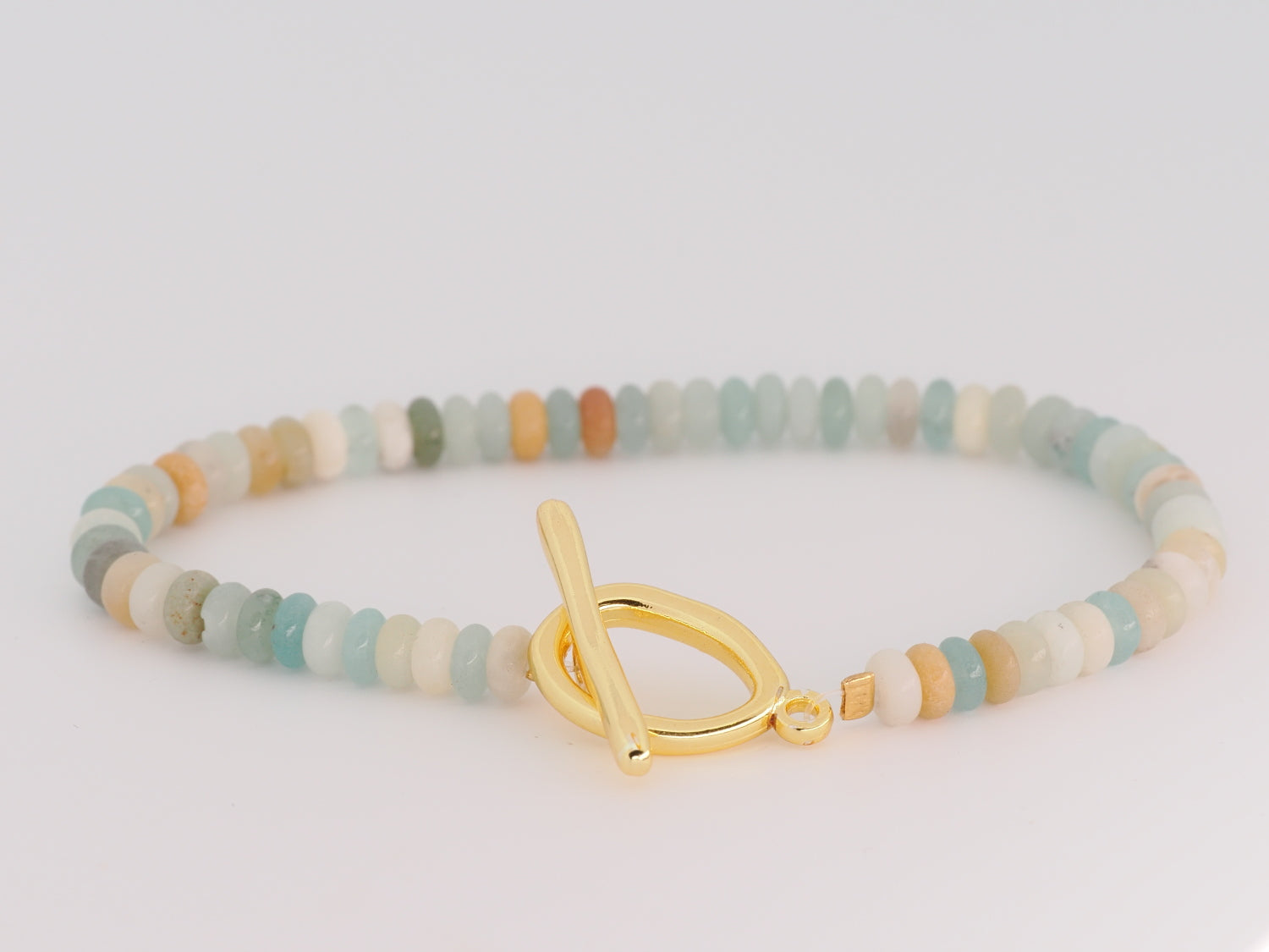 Multicolored beaded bracelet with a gold toggle clasp on a light gray background