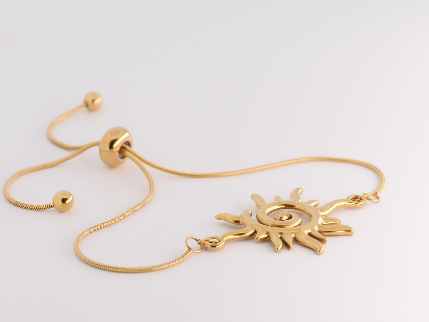 Gold bracelet with sun-shaped clasp on a light gray background