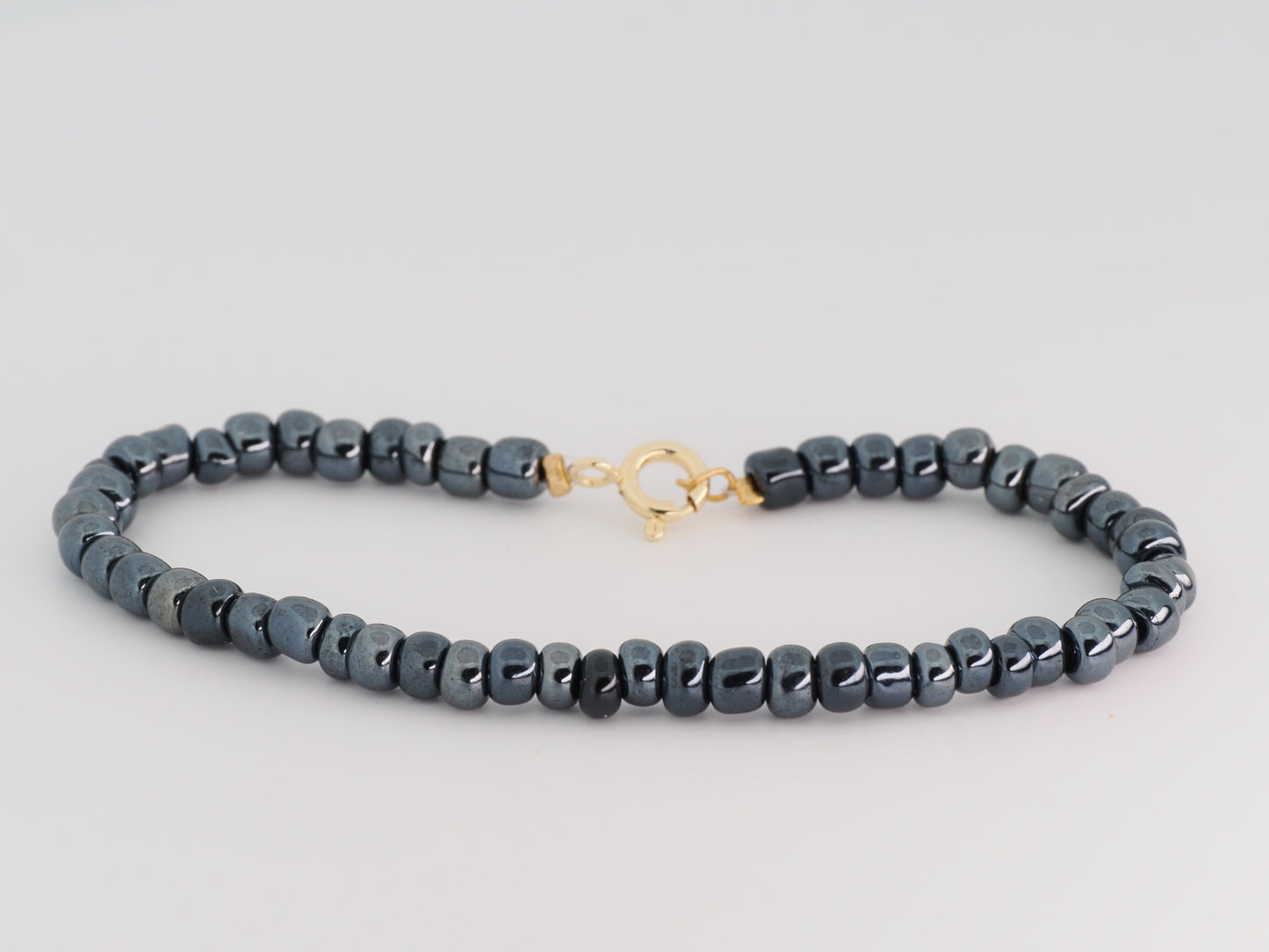 Gray beaded bracelet with a gold clasp on a light gray background