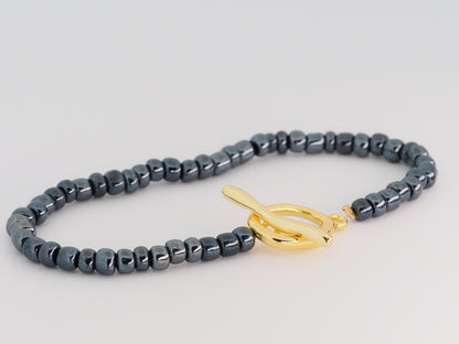 Gray beaded bracelet with a gold clasp on a light gray background