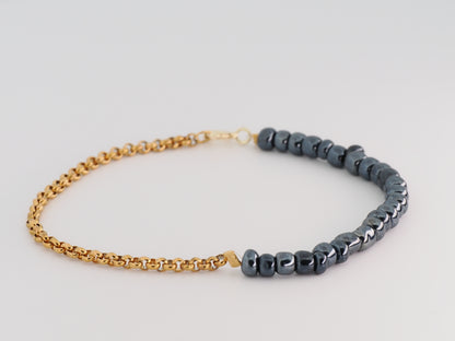 Bracelet with gold chain and dark beads on a light gray background