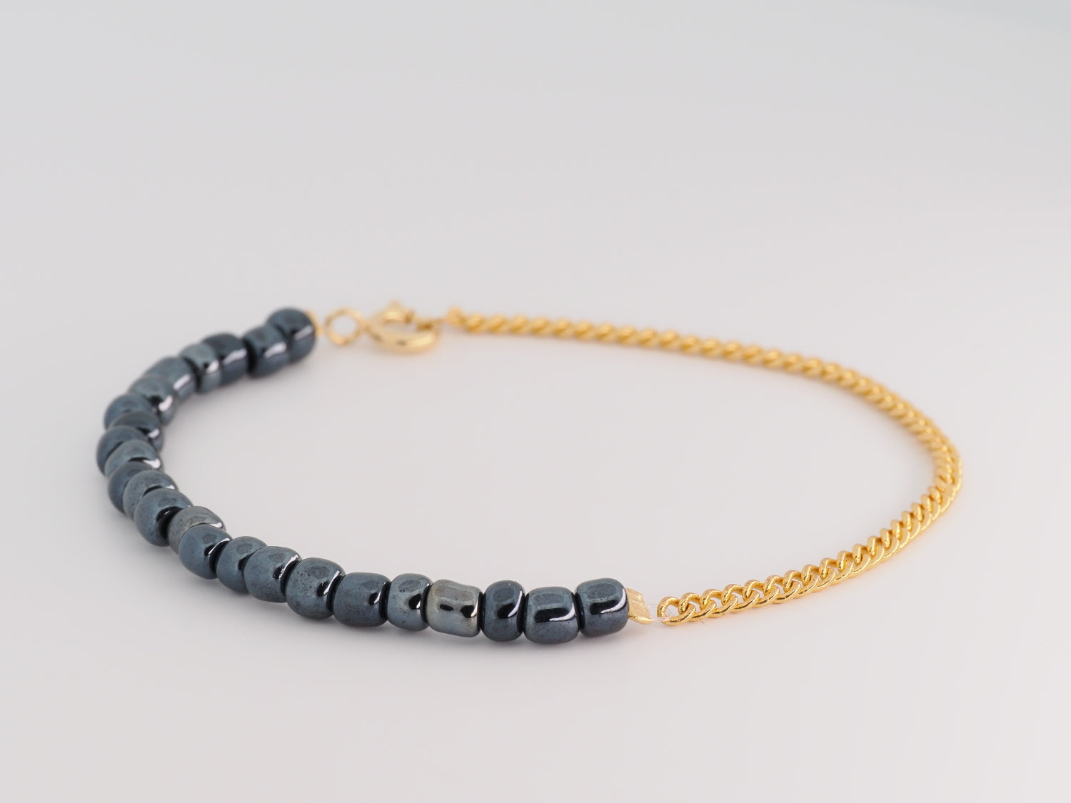 Bracelet with blue beads and gold chain on a light gray background