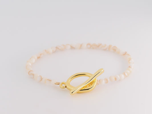 Gold bracelet with a leaf-shaped clasp on a light gray background