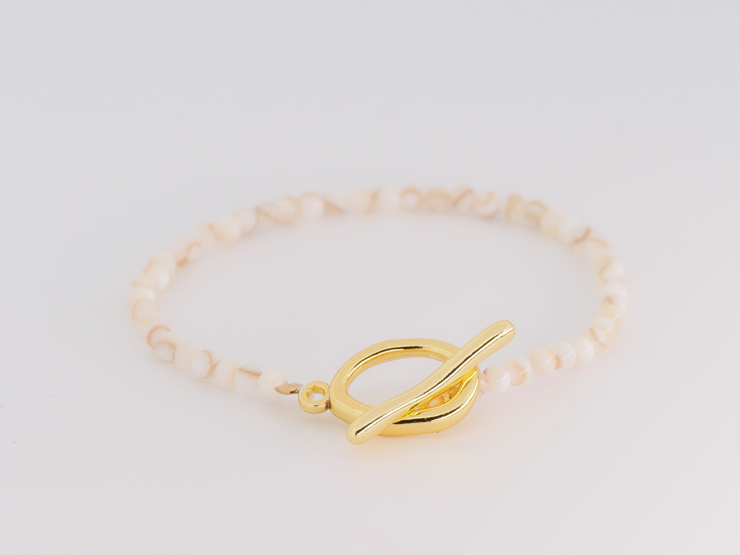 Gold bracelet with a unique clasp on a light gray background