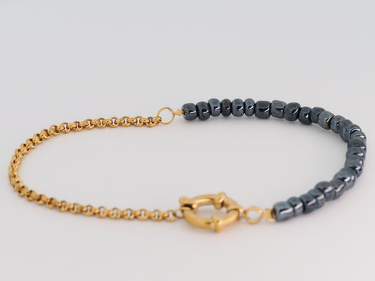 Bracelet with gold chain and dark beaded section on a light gray background
