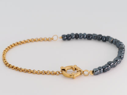 Bracelet with gold chain and gray beaded section on a light gray background