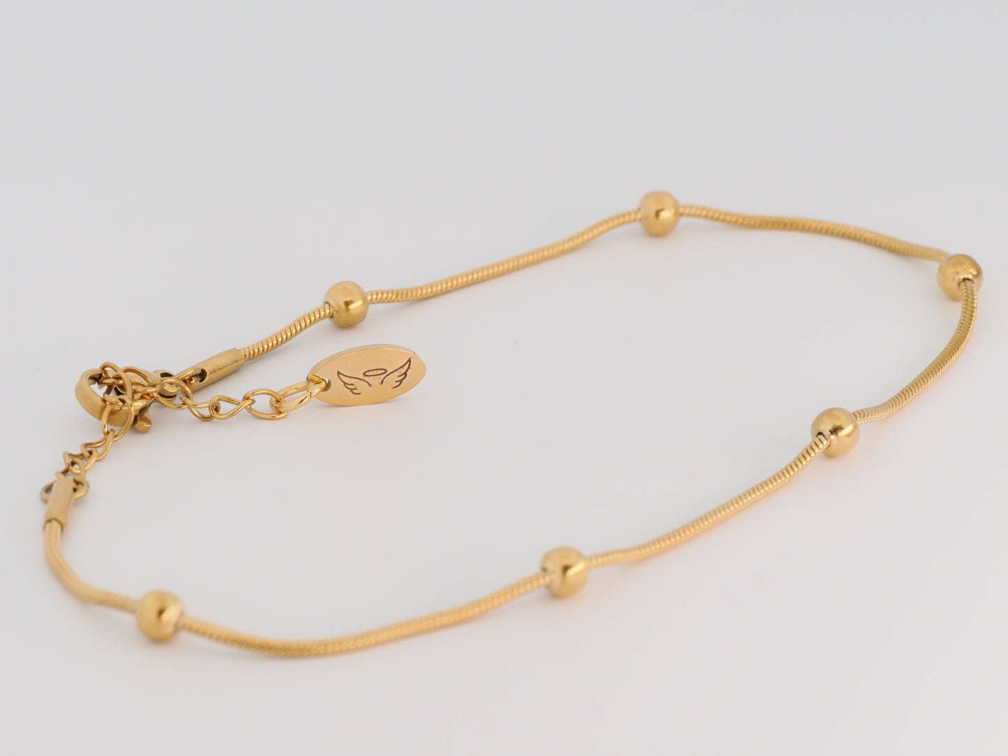 Gold bracelet with small beads on a light gray background