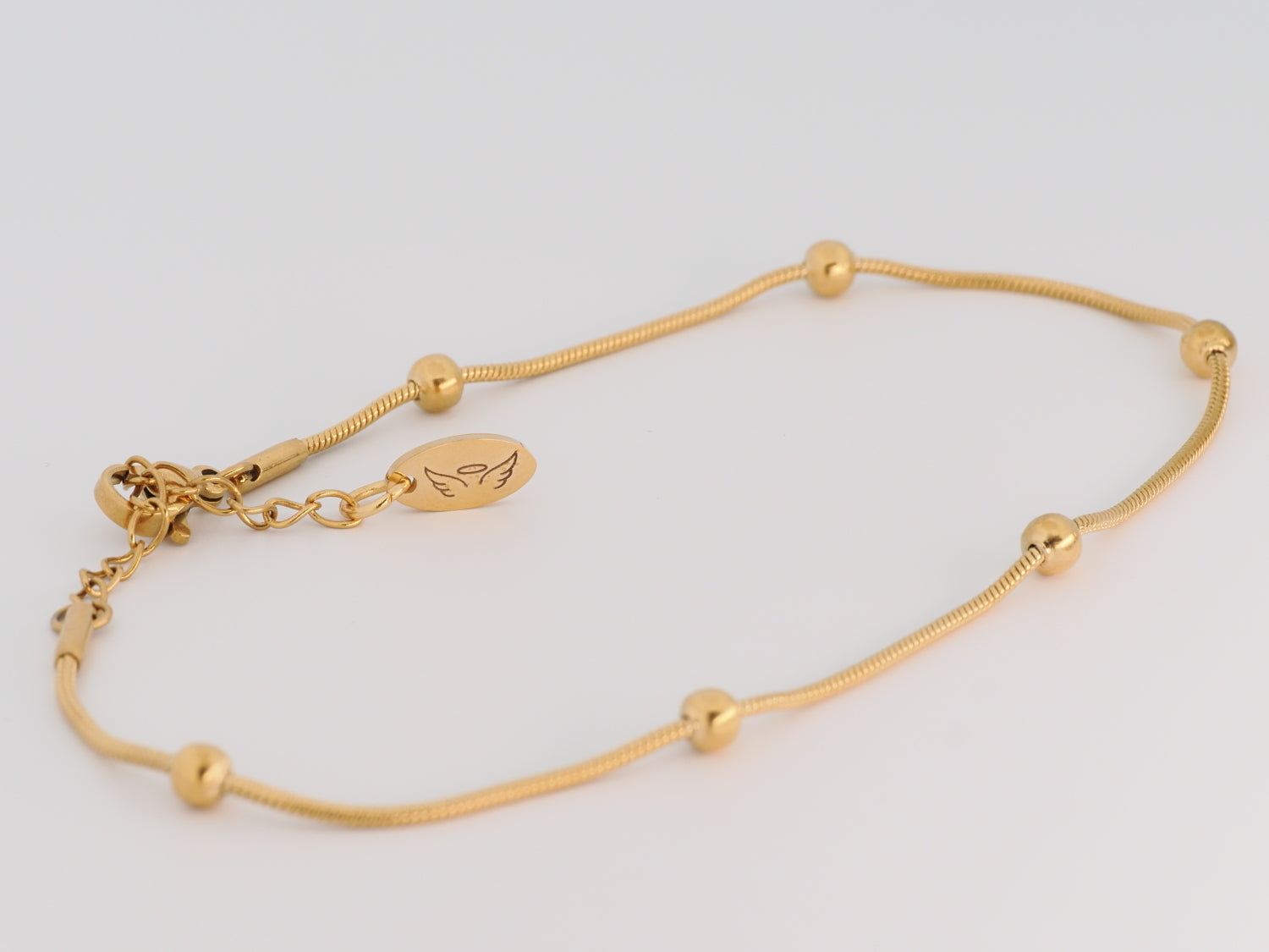 Gold bracelet with small beads on a light gray background