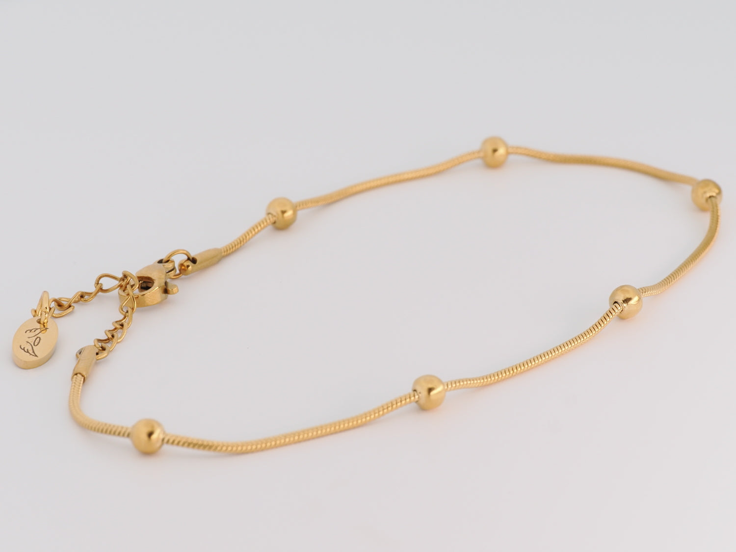 Gold anklet with small beads on a light gray background