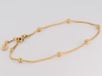 Gold anklet with small beads on a light gray background